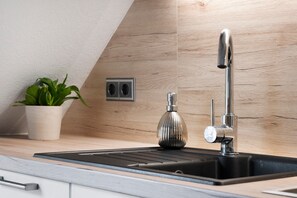 A modern kitchen with a stainless steel sink, a potted plant, and a wooden backsplash.