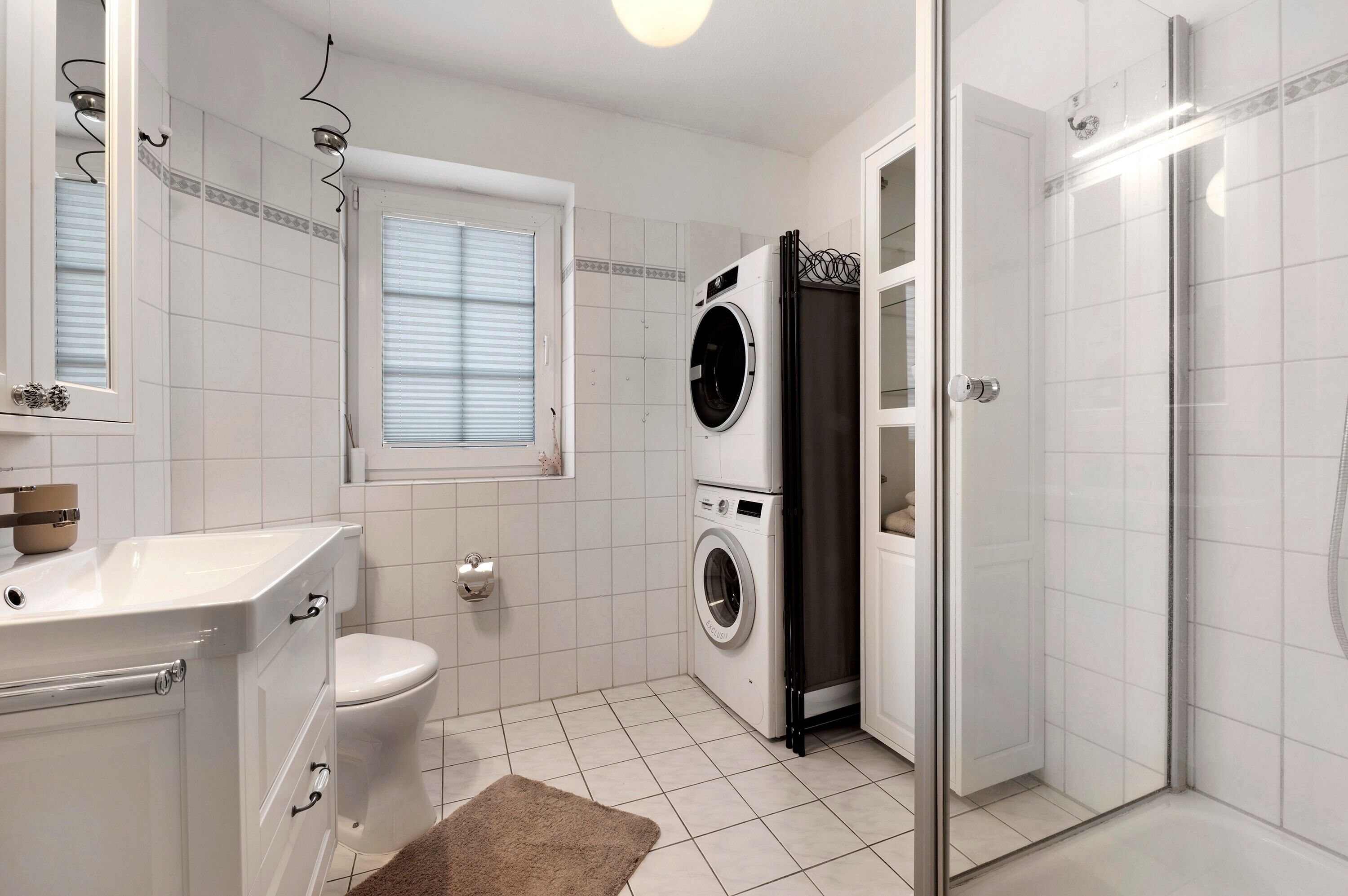 A bathroom with a toilet, a washing machine, a shower, and a sink.