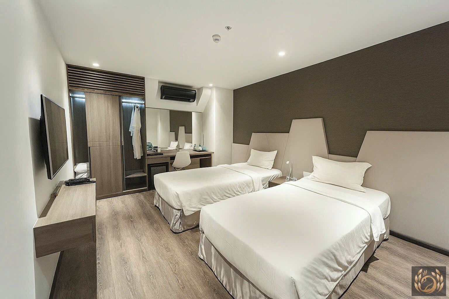 A modern hotel room with two beds, a desk, a chair, a TV, and a large mirror.