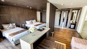 Una habitación de hotel moderna con dos camas, piso de madera, un escritorio con una computadora portátil y un área de comedor con fruta.