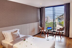 A hotel room with a bed, a desk with a laptop, two chairs, and a large window with a city view. - Brilliant Bay Nha Trang Hotel (Nha Trang)