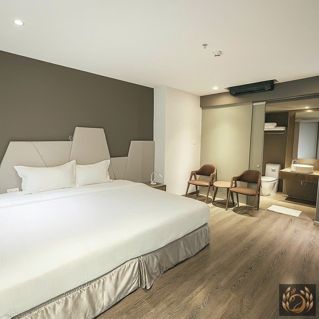 Una habitación de hotel moderna con una cama grande, dos sillones, un escritorio y un baño con espejo y lavamanos.