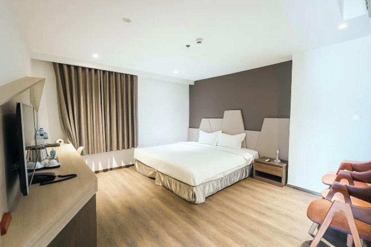 A modern hotel room with a large bed, bedside lamps, a desk with a computer, and a TV.
