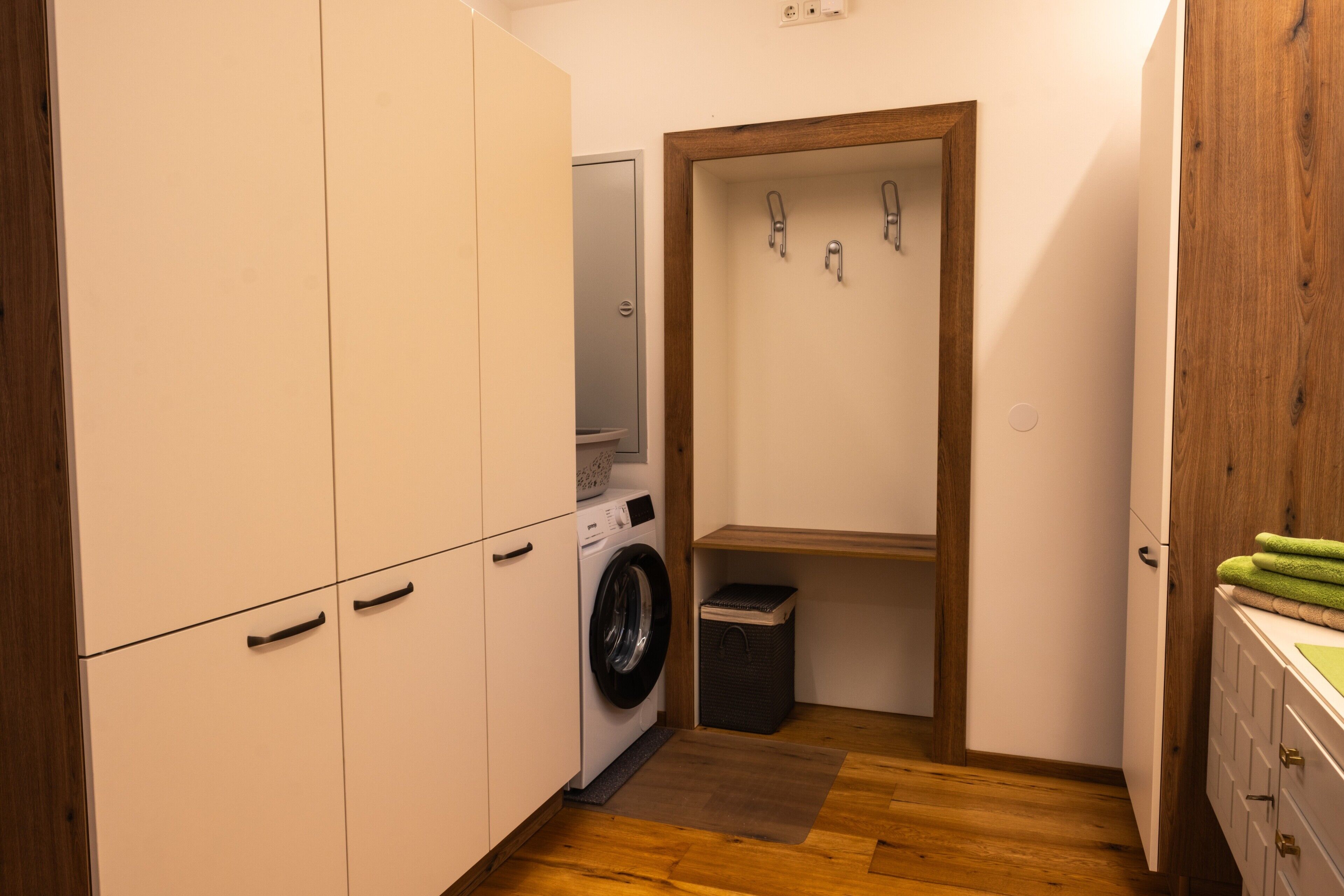 A compact laundry room with a washing machine, a small trash bin, and a wooden door.