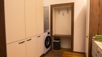A compact laundry room with a washing machine, a small trash bin, and a wooden door.