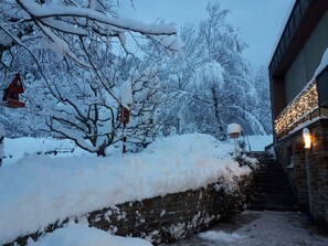 Un espacio exterior cubierto de nieve con un muro de ladrillo, una escalera de madera y un edificio con luces.