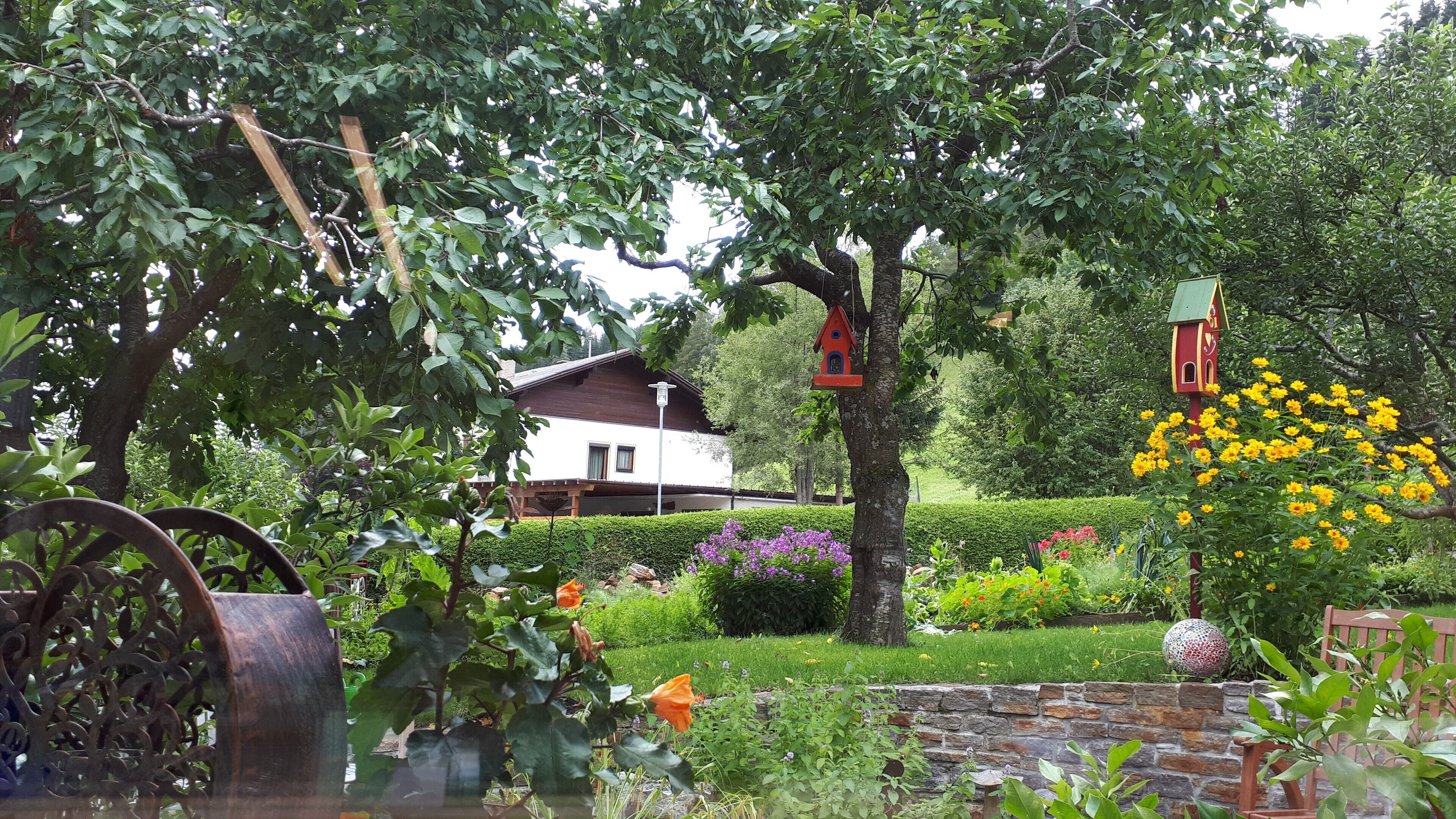 Un giardino con una casa, una scultura in metallo e delle casette per uccelli.
