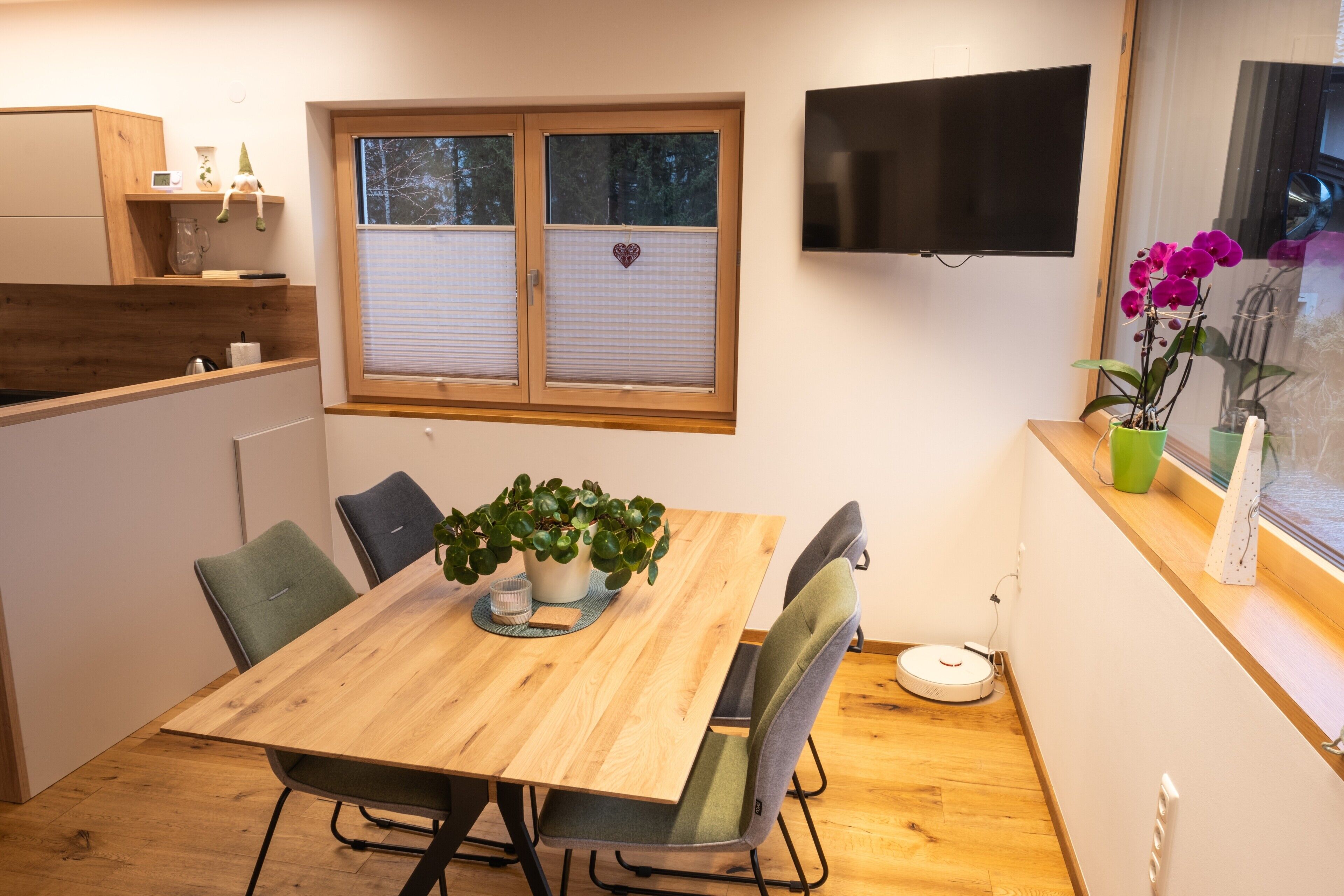 Een moderne keuken met een houten tafel, stoelen, een televisie en een raam met jaloezieën.