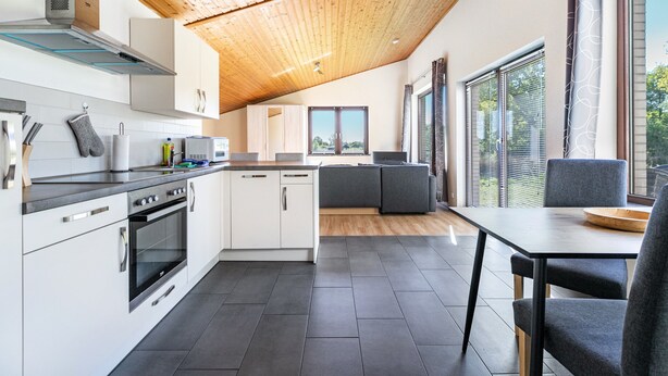A modern kitchen with white cabinets, a built-in oven, and a dining area with a table and chairs.