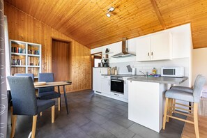 Eine moderne Küche mit Holzbalkendecke, weißen Schränken, einem eingebauten Ofen und einem Essbereich mit grauen Stühlen.