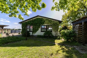Ein kleines Haus mit efeuüberwachsenen Mauern, einem grünen Rasen und einem Holzzaun.
