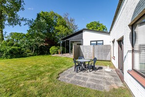 Eine Terrasse mit Tisch und Stühlen, ein überdachter Bereich und ein Gebäude mit Garage.