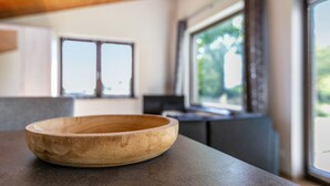A wooden bowl on a countertop in a modern kitchen with large windows and a view of greenery outside.