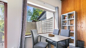 A dining area with a table and chairs, a bookshelf, and a window with curtains.