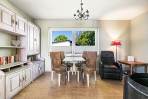 A dining area with a table, chairs, a chandelier, a red lamp, and a view through a window. - Holiday Apartment 'Wiesenblick 1' with Private Terrace, Private Garden and Wi-Fi (Weddingstedt)