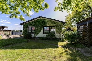 A small house with ivy-covered walls, a grassy yard, and a wooden fence. - Holiday Apartment 'Wiesenblick 1' with Private Terrace, Private Garden and Wi-Fi (Weddingstedt)