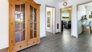 A spacious hallway with a wooden cabinet, a kitchen area with a dining set, and a view of the outdoors.