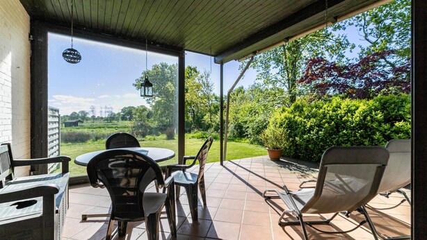 An outdoor patio with a table and chairs, a hanging lantern, and a view of a garden and trees.