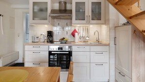 A modern kitchen with white cabinets, a stainless steel range hood, a built-in oven, and a wooden dining table. - Apartment 'Hafenambiente' with Private Terrace and Wi-Fi (Husum)