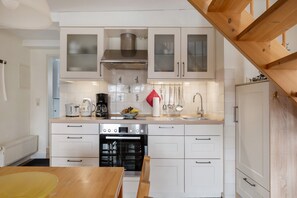 A modern kitchen with white cabinets, a stainless steel range hood, a built-in oven, and a wooden dining table.