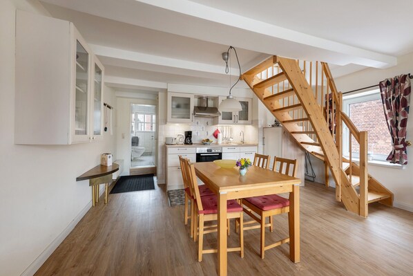 A modern kitchen with white cabinets, a wooden staircase, and a dining area with a wooden table and chairs.