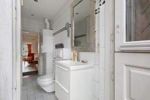 Une salle de bain équipée de toilettes, d’un lavabo, d’un miroir et d’un porte-serviettes.
