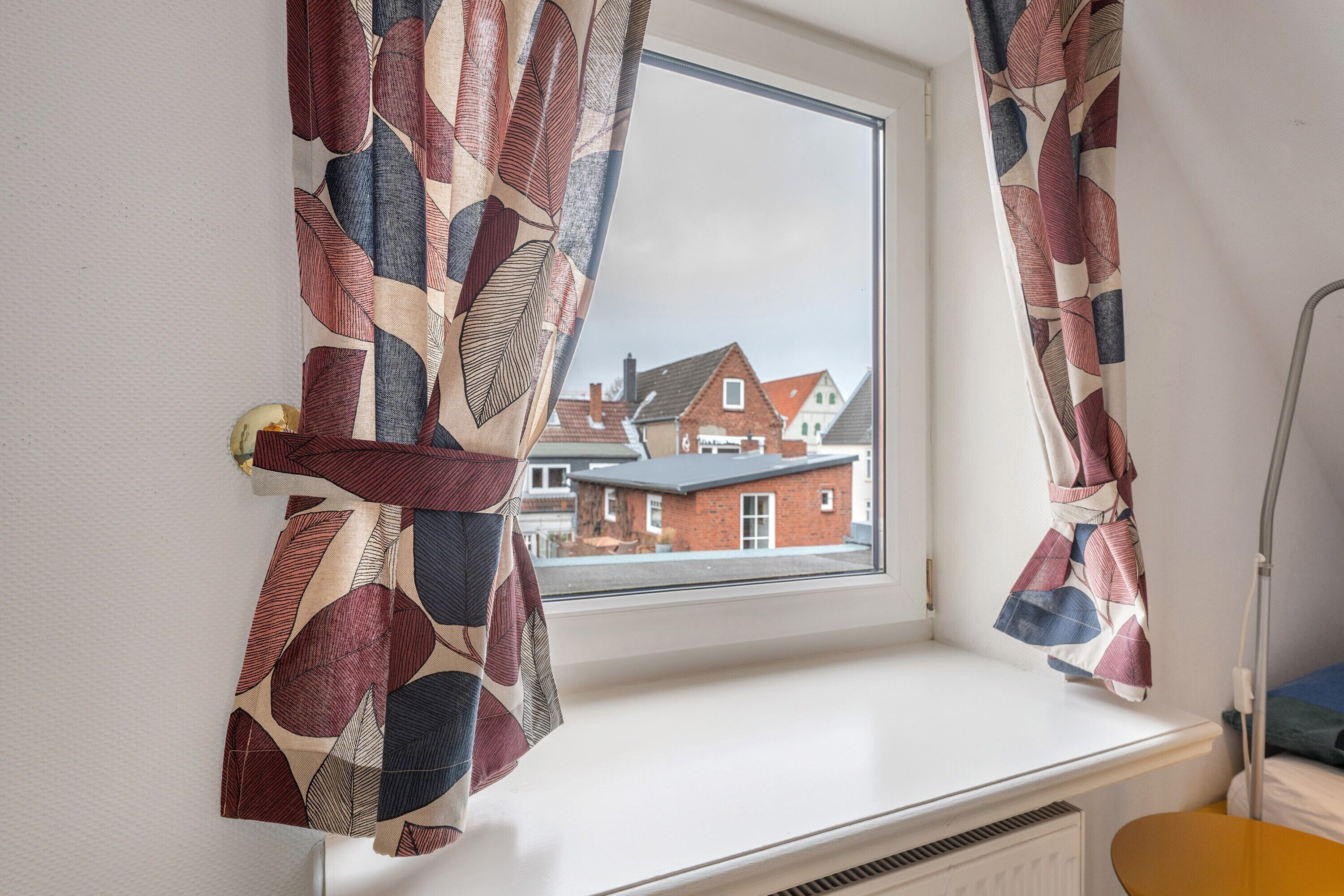 A room with a window, a radiator, and a view of houses.