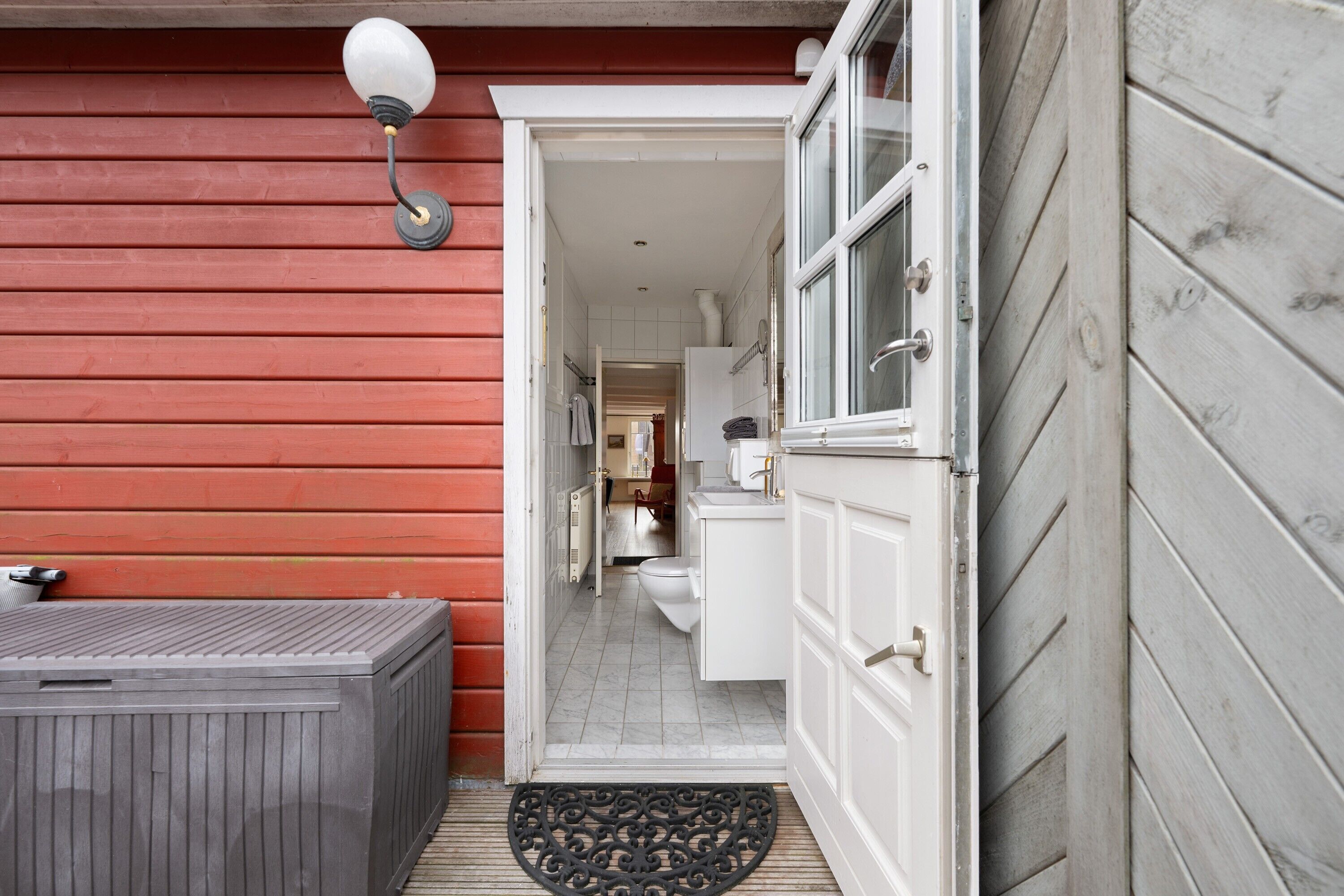 A wooden exterior with a door leading to a bathroom and a small outdoor seating area.
