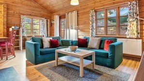 A cozy cabin with a wooden interior, a green sofa, a wooden coffee table, and large windows with curtains. - Apartment 'Johanna' with Private Terrace, Private Garden and Wi-Fi (Zislow)