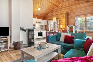 Un intérieur de chalet chaleureux avec un plafond en bois, un coin repas, un canapé, une télévision et une cuisine.
