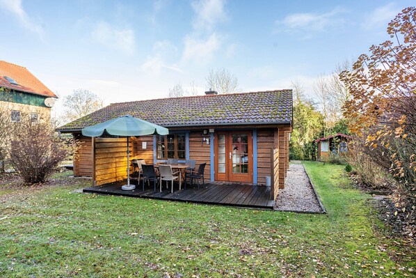 Una casa de madera con un patio, una mesa con sillas y un área cubierta con un paraguas.