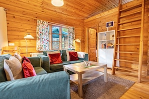L’intérieur d’un chalet accueillant, avec un plafond en bois, un canapé agrémenté de coussins, une table avec un vase et une bibliothèque.