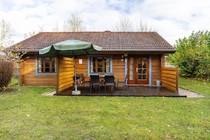 Une cabane en bois avec un toit en tuiles, une terrasse avec des chaises et une table, et un espace extérieur couvert.