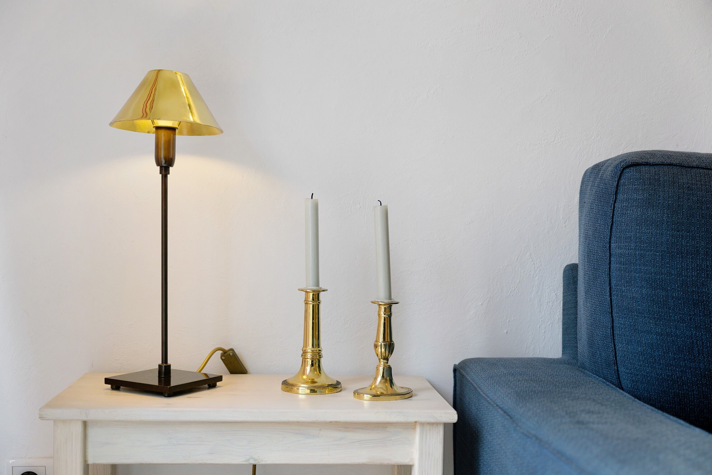 A white bedside table with a lamp and two candle holders.