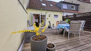 Eine Terrasse mit Tisch und Stühlen, einem Blumentopf und einem Gebäude mit Ziegeldach.