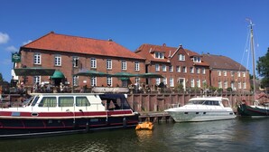 Een historisch gebouw met een rood pannendak, een steiger met boten, en een heldere blauwe lucht.