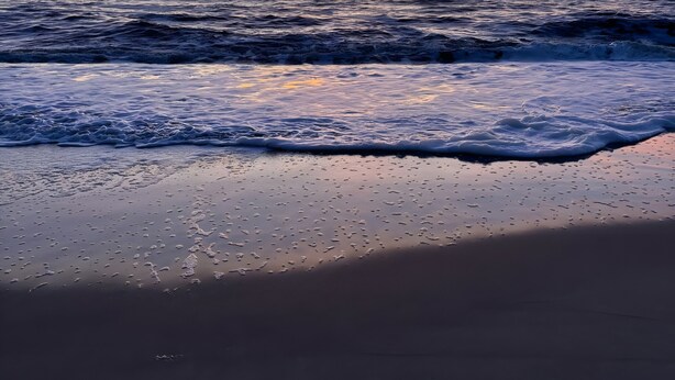Een strand met golven en een zonsondergang.