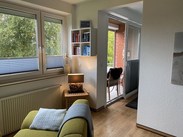 Une pièce comprenant un canapé, une petite table avec une lampe, une bibliothèque et une vue sur l’extérieur grâce à une porte coulissante.