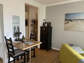 Un espace de vie compact comprenant un coin repas, une kitchenette, un canapé et un tableau au mur.