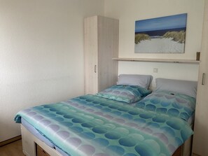 A single bed with a patterned bedspread, a wardrobe, and a painting of a beach scene above the bed. - Apartment 'Felix, 35qm' with Balcony (Horumersiel-Schillig)