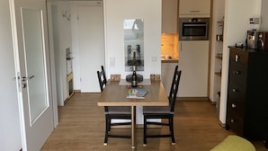 Een ruimtelijk ingerichte leefruimte met een eethoek, een kitchenette en een deur naar een andere kamer.
