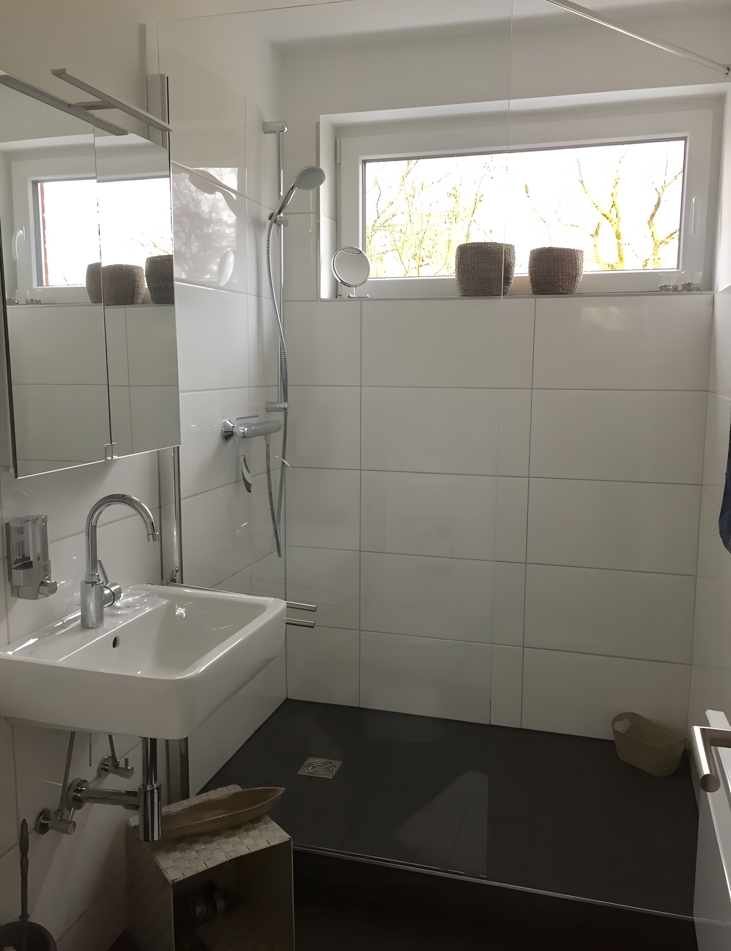 Ein modernes Badezimmer mit Waschbecken, Spiegel, Dusche und Fenster mit Blick auf Bäume.