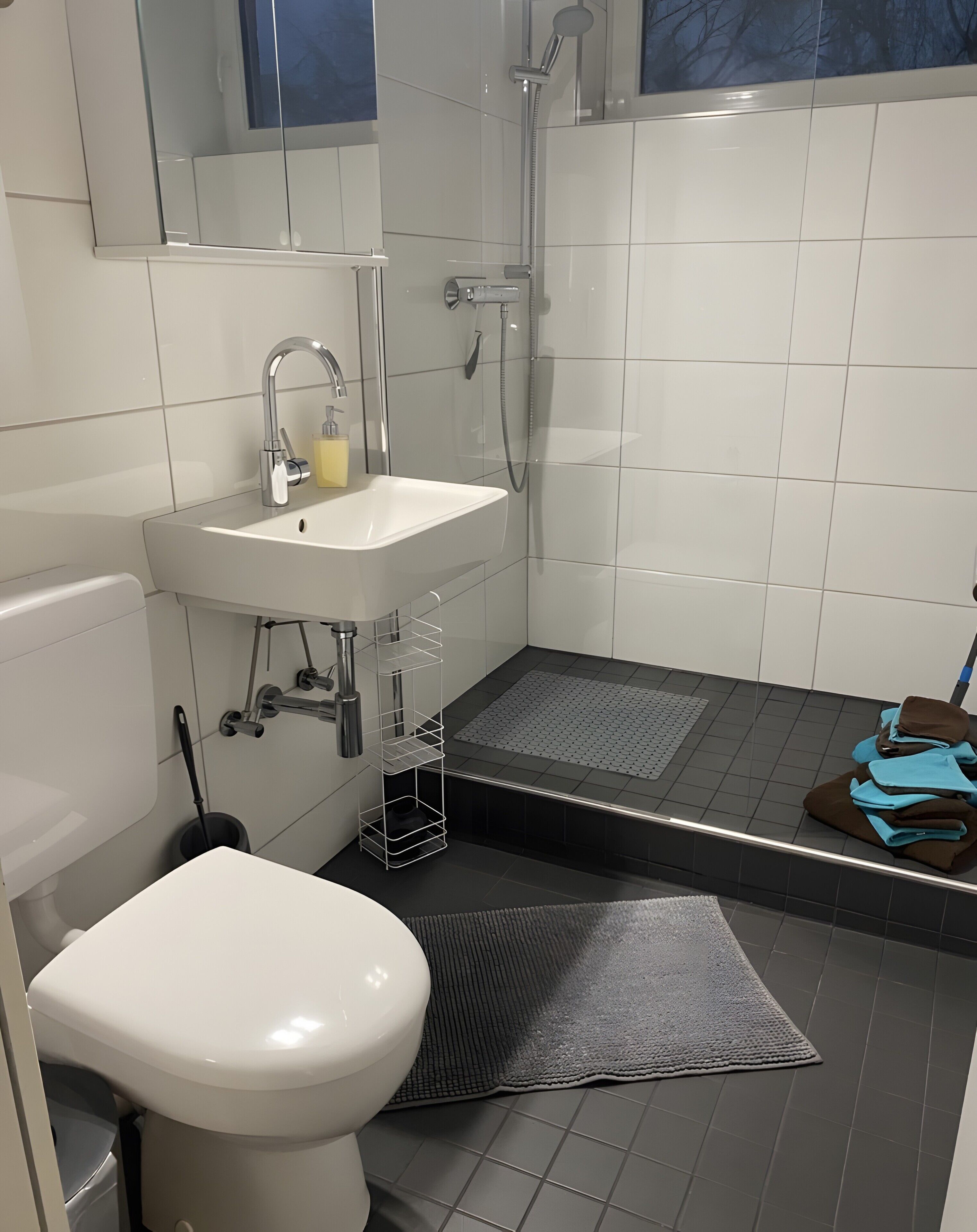 Ein modernes Badezimmer mit Waschbecken, Toilette und Dusche, alles in Weiß.