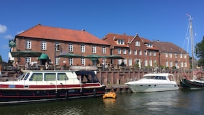 A historic building with a red-tiled roof, a dock with boats, and a clear blue sky. - Apartment 'Jan, 35qm' with Balcony (Horumersiel-Schillig)