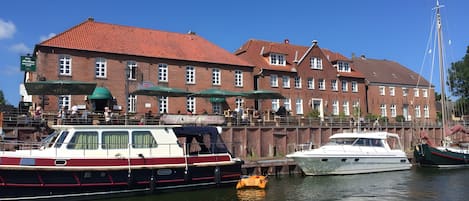 En historisk bygning med rødt tegltag, en bro med både og en klar blå himmel.