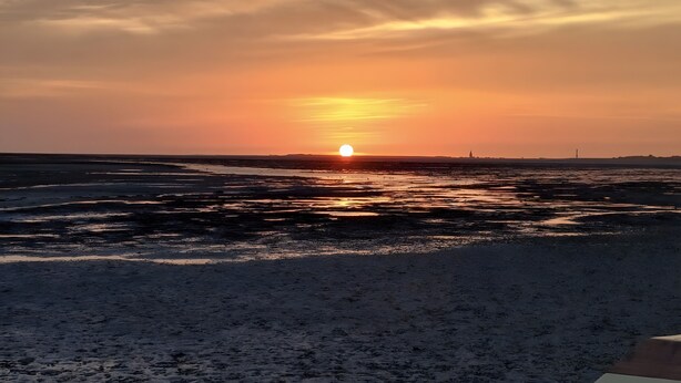 A sunset over a beach with a distant view of a city skyline. - Apartment 'Jan, 35qm' with Balcony (Horumersiel-Schillig)