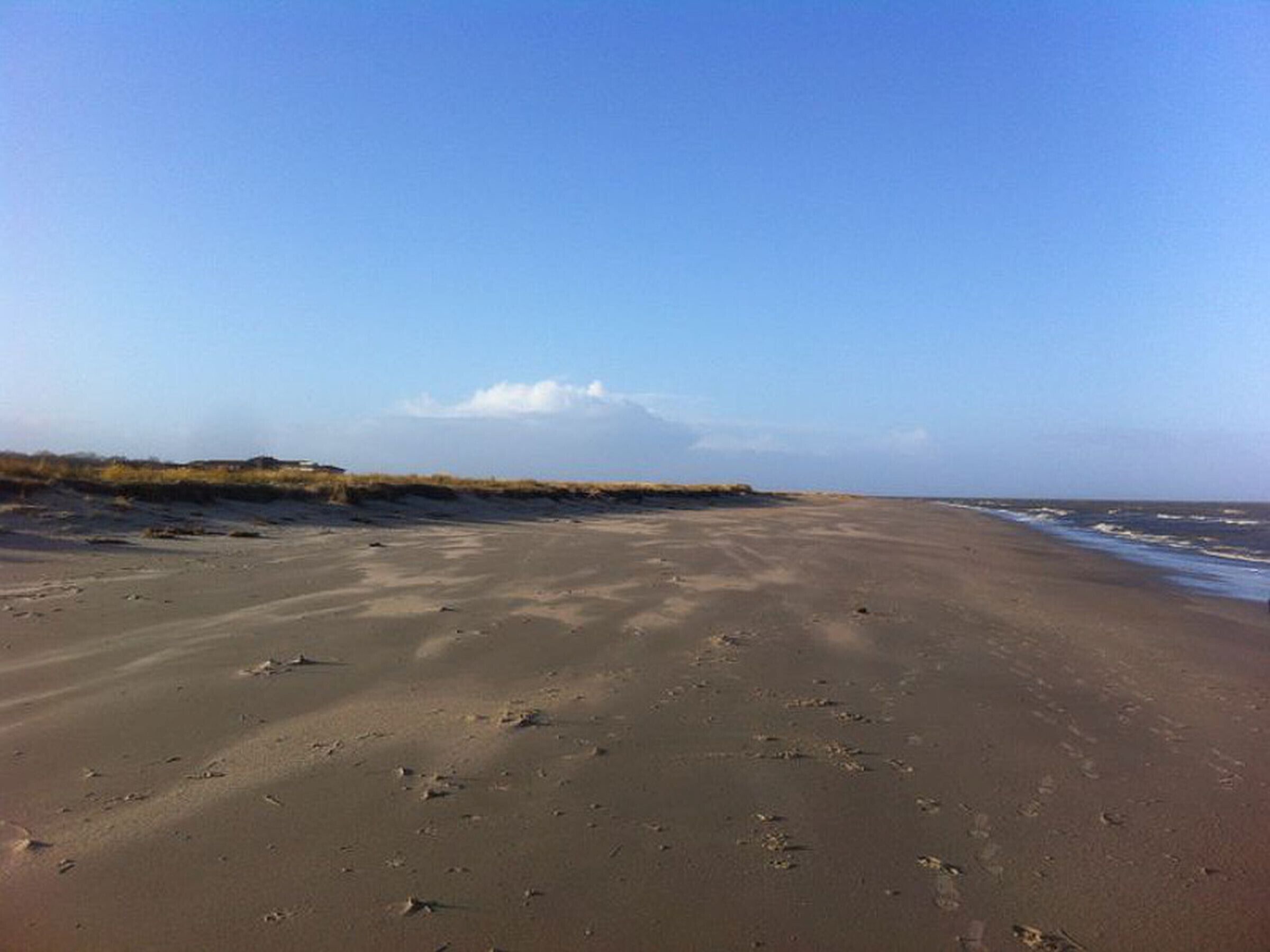 Een breed zandstrand met voetafdrukken en een heldere lucht.