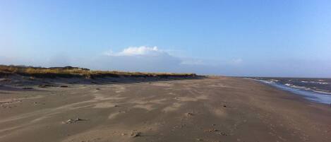 Een breed zandstrand met voetafdrukken en een heldere lucht.