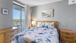 Een slaapkamer met een bed, nachtkastje, dressoir, raam met gordijnen en een plafondventilator.