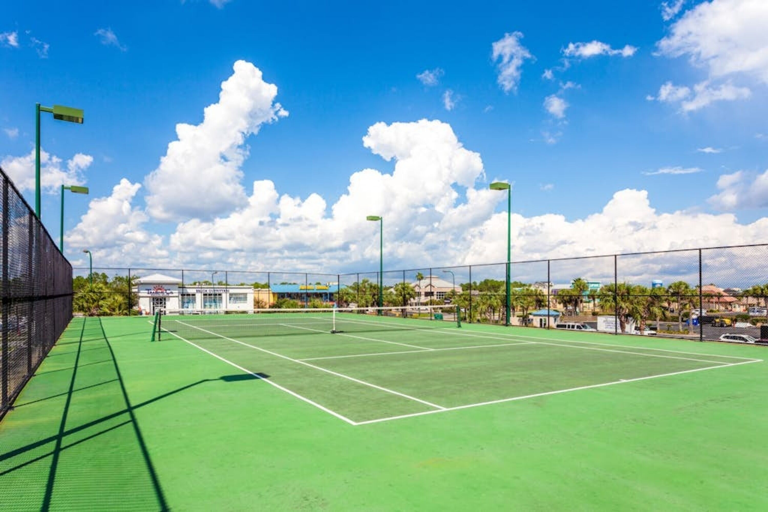 Ein Tennisplatz im Freien mit grüner Belag, umgeben von einem Zaun und unter blauem Himmel.